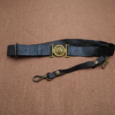 une ceinture en cuir noir avec une boucle en laiton sur fond marron