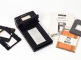 un petit appareil photo et quelques autres objets posés sur une surface blanche