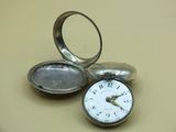 a silver pocket watch sitting on a table with a ring on it