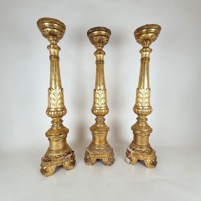 three gold candlesticks on a white surface with a white background