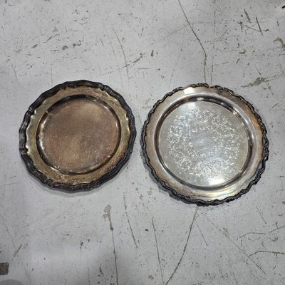 two silver plates sitting on a table next to each other