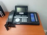 un téléphone noir posé sur un bureau en bois, à côté d'un haut-parleur