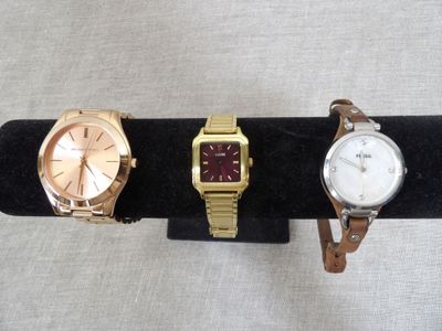 three watches on a black display stand with a white background