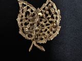 a close up of a gold brooch with a leaf on it