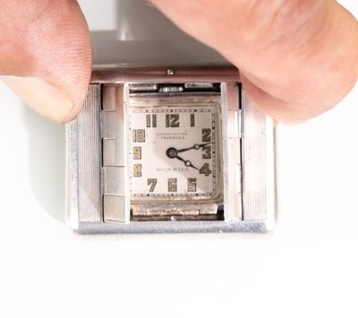a person holding a small square watch in their hand