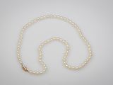 un collier de perles blanches avec un fermoir en or sur fond blanc