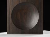 un objet en bois posé sur une surface blanche, sur fond noir