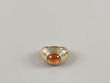 une bague en or sertie d'une pierre orange repose sur une surface blanche