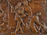 a bronze relief of a man with a rifle and a dog