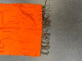 an orange scarf with fringes laying on the ground