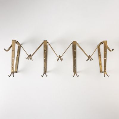 trois crochets en laiton sont accrochés en rangée sur un mur, sur fond blanc