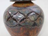 a brown and black vase with a lid on a white surface