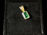 a close up of a green and gold pendant in a black box