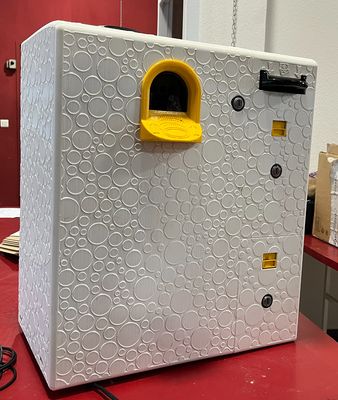 une boîte blanche munie d'une poignée jaune, posée sur une table rouge