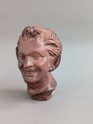 statue représentant la tête d'une femme aux cheveux bouclés, posée sur une surface grise