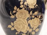 a black vase with gold flowers on it sitting on a table