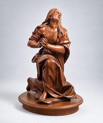 une statue en bronze de Jésus tenant la croix, posée sur un socle en bois
