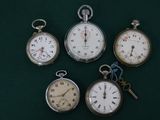 Plusieurs modèles différents de montres de poche sont exposés sur un fond vert