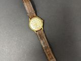 une montre en or avec un bracelet marron sur un fond noir