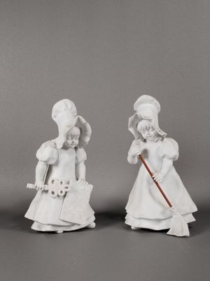 deux figurines blanches représentant des femmes portant un chapeau et une canne