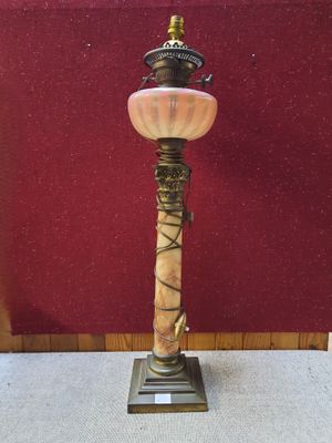 lampe en laiton et marbre posée sur un socle, avec un mur rouge en arrière-plan