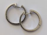 une paire de boucles d'oreilles créoles en argent ornées de petites pointes, sur un fond blanc