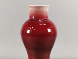un vase rouge avec un couvercle blanc posé sur une table