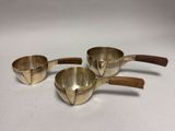 three brass measuring cups with wooden handles on a white surface