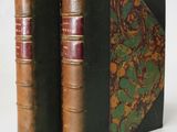 two old books sitting on top of each other on a white surface