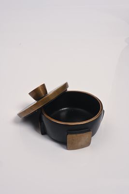 un bol noir avec un couvercle doré posé sur une surface blanche
