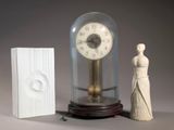 une horloge sous un dôme de verre, à côté d'une petite statue