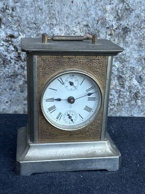 a small silver clock with roman numerals on it