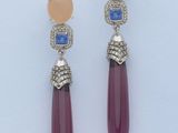 une paire de boucles d'oreilles ornées de pierres roses et bleues sur un fond blanc