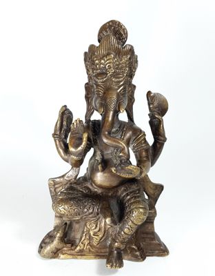 brass statue of ganesh sitting on a rock with two hands raised