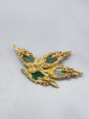 un gros plan d'une broche en or ornée de pierres vertes