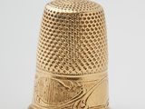 an antique gold thimble on a white surface