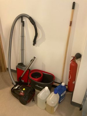 une photo d'une pièce où l'on voit un aspirateur, un seau, une serpillière et d'autres produits d'entretien
