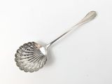 une cuillère en argent dont le manche a la forme d'un coquillage, posée sur une surface blanche