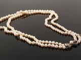 a white pearl necklace with a diamond clasp on a black surface