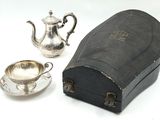 une théière en argent et une tasse en argent posées sur une table blanche