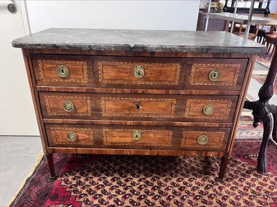 a wooden chest of drawers with marble top on a rug