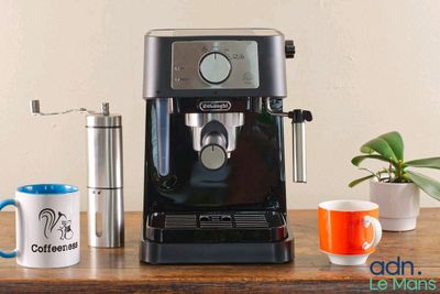 a black coffee machine sitting on a wooden table next to two cups