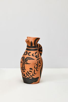 un vase orange et noir posé sur une table blanche
