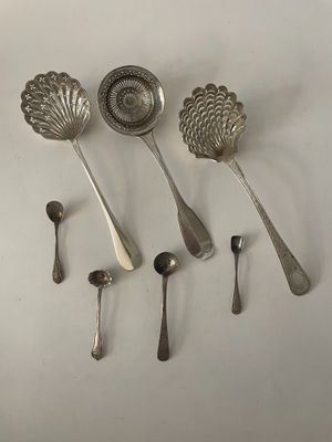 six cuillères en argent et une cuillère doseuse posées sur un plan de travail blanc