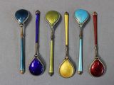 six cuillères de couleurs différentes sont alignées sur une surface grise