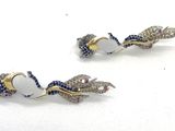 une paire de boucles d'oreilles blanches et bleues rehaussées de touches dorées sur un fond blanc