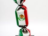 bonbon emballé dans le drapeau mexicain, posé sur un support noir devant un fond blanc