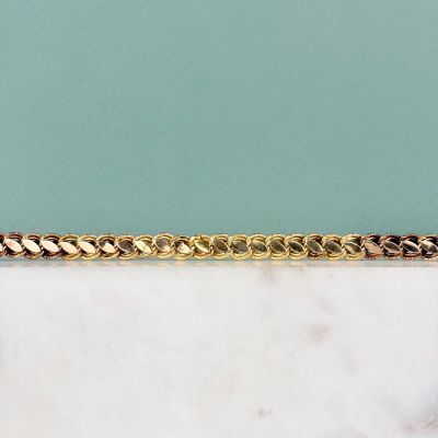 Le bracelet en chaîne d'or est posé sur une dalle de marbre.