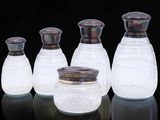 quatre bocaux en verre munis de couvercles argentés sont alignés sur une surface noire