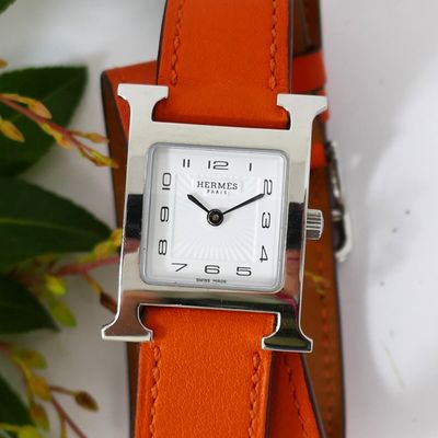 a small square watch with a silver face on a orange strap